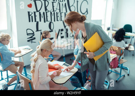 Teacher checking exercises in copybooks of her pupils. Stock Photo