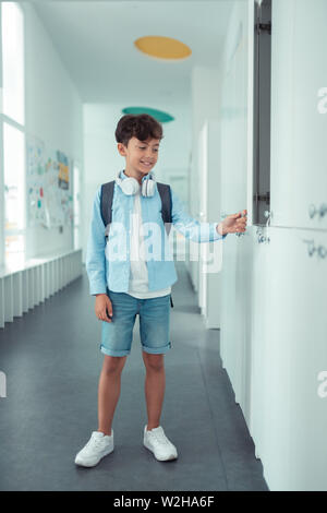 Schoolboy wearing denim shorts standing near school locker Stock Photo
