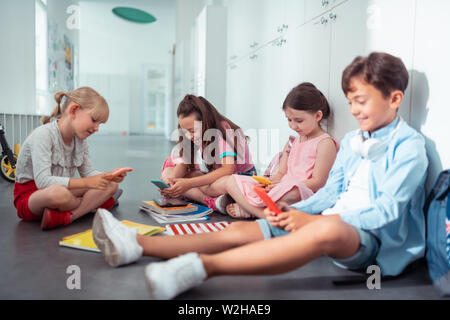 Children addicted to smartphones using them during break at school Stock Photo