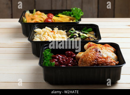 three black food boxes with boiled beans, baked chicken wings and steamed vegetables Stock Photo