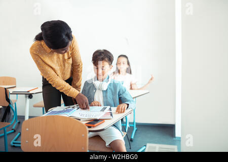 Dark-skinned teacher standing near handsome smart pupil Stock Photo