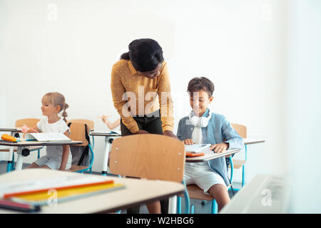 Dark-haired boy smiling while speaking with teacher Stock Photo
