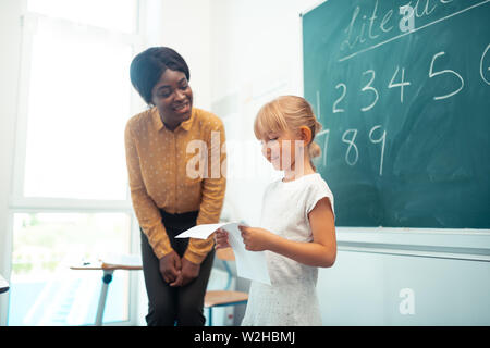 Dark-skinned teacher speaking with pupil near blackboard Stock Photo