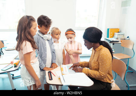 Girls and boy standing near their teacher telling them test results Stock Photo