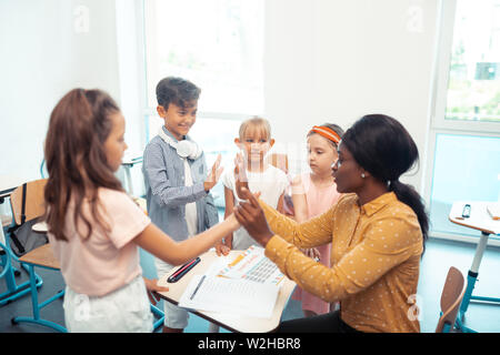 Dark-skinned teacher giving high five to her smart cute pupils Stock Photo