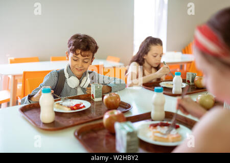 Schoolchildren having yummy lunch in canteen together Stock Photo