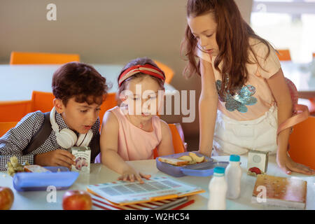 Girls and boy checking the schedule while having lunch in canteen Stock Photo