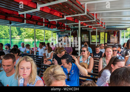 Tourists on a ferry navigating on the turquoise colored crystal clear and pure water of Lake Kozjak, Plitvice Lakes National Park, Croatia Stock Photo