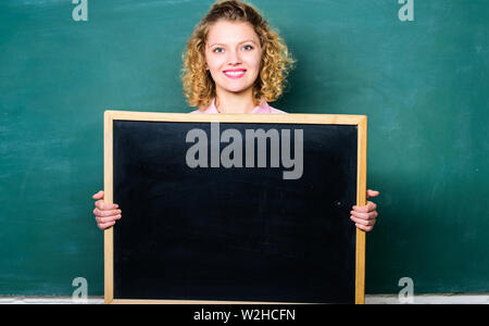 Well Done is Our Duty. woman teacher at blackboard. copy space. here is your advertisement. informations board. announcement concept. place to write task. happy student girl hold blank board. Stock Photo