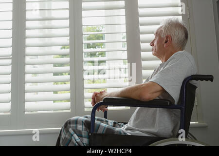 Active senior man in wheelchair looking through window at home Stock Photo