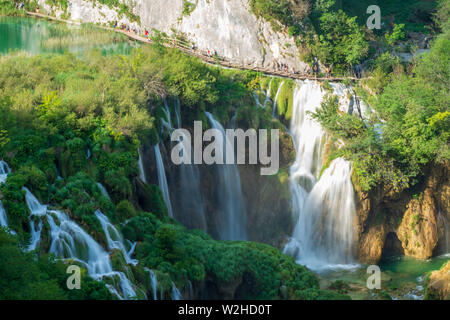 Tourists walking along the wooden boardwalk above the Large Waterfall at the Plitvice Lakes National Park in Croatia Stock Photo