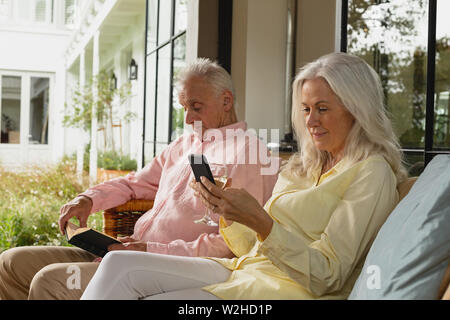 Active senior couple using mobile phone and reading a book in the porch Stock Photo