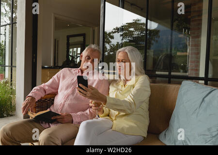 Active senior couple using mobile phone and reading a book in the porch Stock Photo