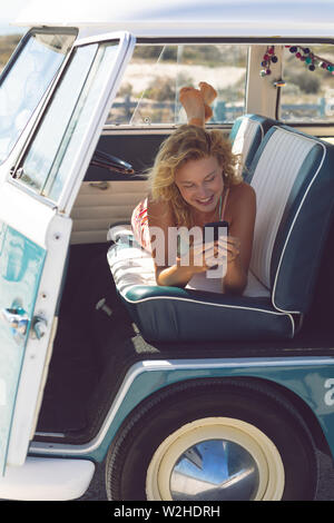 Woman using mobile phone while lying on seat in camper van at beach Stock Photo