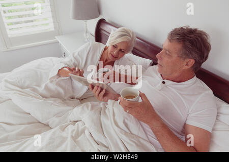 Active senior couple using digital tablet while having coffee together in bed in bedroom Stock Photo
