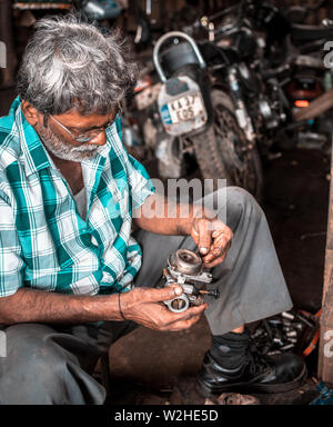 Mechanic repairing a carburettor on a motorcycle in a small workshop in rural India Stock Photo