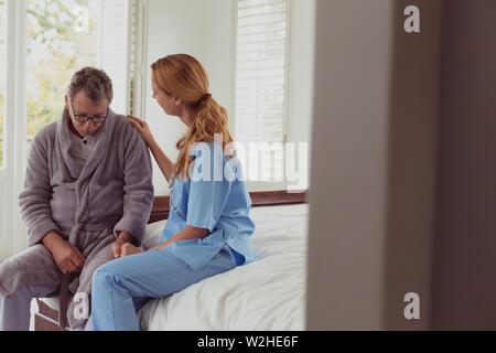 Female doctor consoling active senior man in a comfortable home Stock Photo