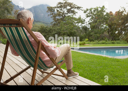 Active senior man reading a book while relaxing on sun lounger in the backyard Stock Photo