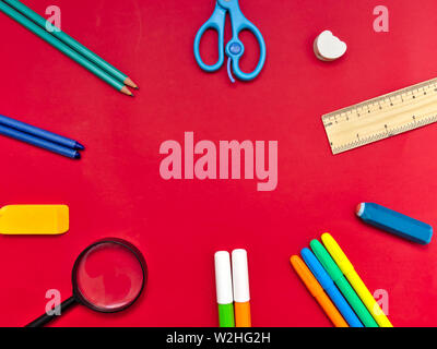 Colorful school supplies in circle arrangement on red background, back to school concept. Stock Photo