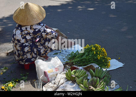 Hanoi, Vietnam, April 3, 2019: A vietnamese woman seated on the road sells yellow flowers. Woman Vendor of flowers on the street of Ha Noi, Vietnam. Stock Photo