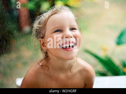 Close up portrait of happy cute little girl enjoy summer rain.  Drops fall on her face, child smiling. childhood, emotions and vacation concept Stock Photo