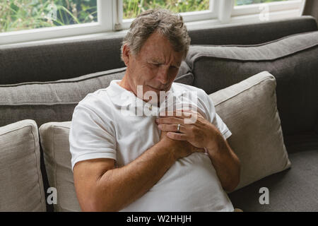 Active senior man suffering from chest pain on sofa in a comfortable home Stock Photo