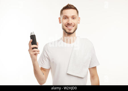 Young bearded man on the white background looks at the male deodorant in a black bottle. Stock Photo
