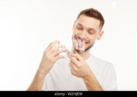 Young man on the white background does his own manicure with several tools. Stock Photo