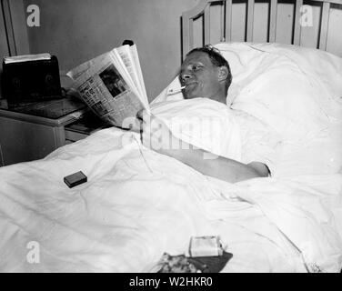 Man in hospital bed smoking a cigarette while reading a newspaper