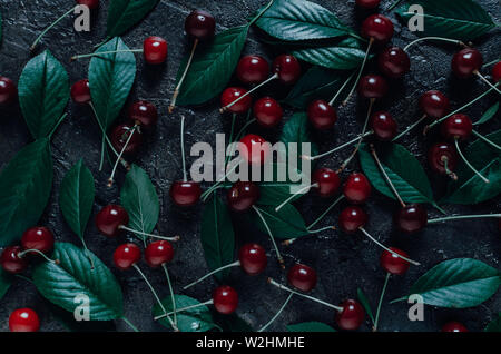 Ripe, bright cherry with green leaves on an old, rustic stone background with a view from the top. Stock Photo