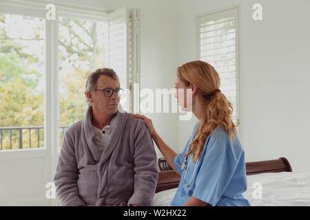 Female doctor consoling active senior man in a comfortable home Stock Photo