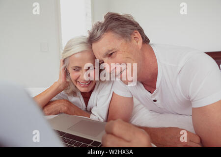 Active senior couple using laptop while lying on bed in bedroom at comfortable home Stock Photo