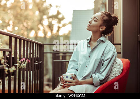 Peaceful good-looking woman in oversize male shirt carrying big cup Stock Photo