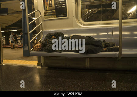 A homeless man sleeps on a subway seat in New York City Note other ...