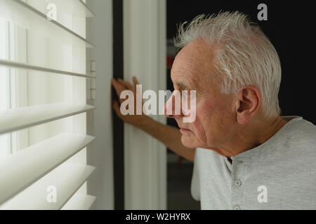 Active senior man looking through window at home Stock Photo