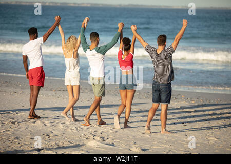 Group of friends standing with raised hands on the beach Stock Photo