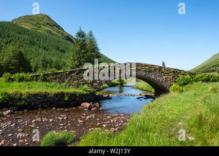 Tourist crossing Butterbridge, an old stone single arched bridge, over Kinglas Water in Glen Kinglas, Argyll and Bute, Scotland, UK Stock Photo