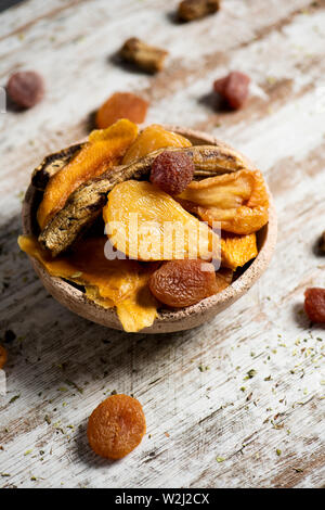 closeup of a rustic earthenware bowl full of assorted dried fruit, such as pear, peach, banana, strawberry, apple or apricot, on a white rustic wooden Stock Photo