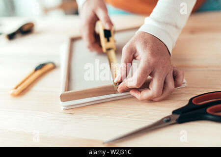 Female carpenter tape measuring picture frame in small business woodwork workshop, close up of hands Stock Photo