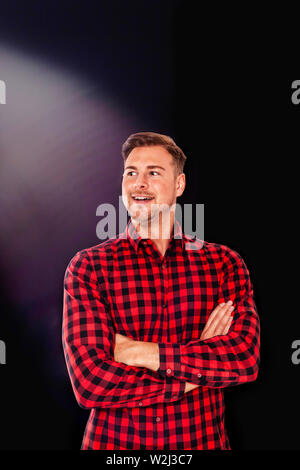 Confident bearded man with a cheerful smile standing with folded arms looking aside watching over dark grey with copy space Stock Photo