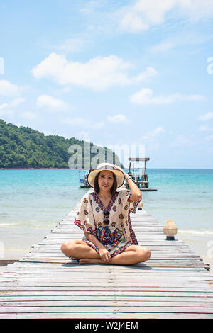 Women Wear a hat on the wooden bridge pier boat in the sea and the bright sky at Koh Kood, Trat in Thailand. Stock Photo