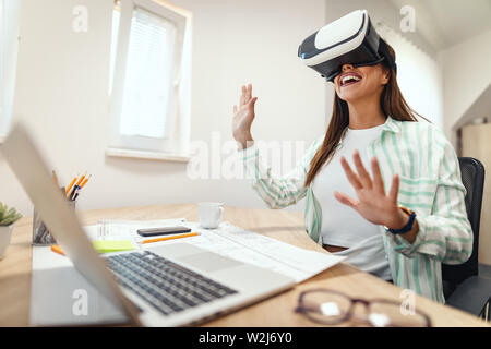 Smiling businesswoman is using virtual reality glasses. She is having fun with new technology console online. Stock Photo