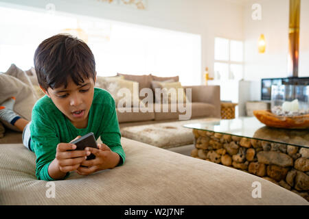 Boy using mobile phone while lying on sofa at home Stock Photo