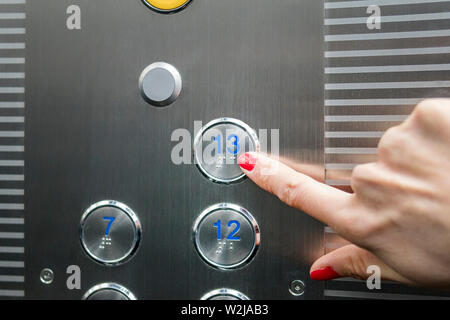 Woman in elevator or lift is pressing the button to get into the right floor only hand to be seen - close-up. 13 th floor Stock Photo