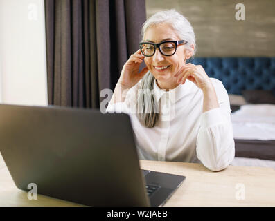 Senior long haired woman wearing glasses using videochat and has pleasant talking Stock Photo