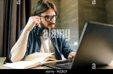 Bearded student man in headphones wearing glasses using laptop at the evening at the flat Stock Photo