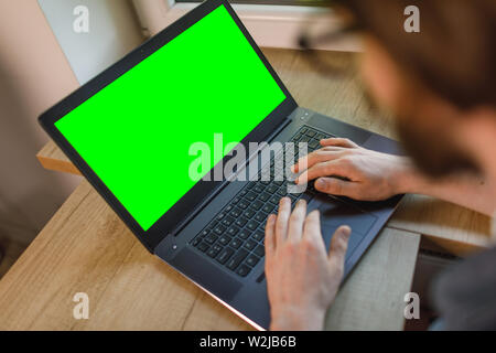 Bearded man is working using laptop at his flat, blank screen for background Stock Photo