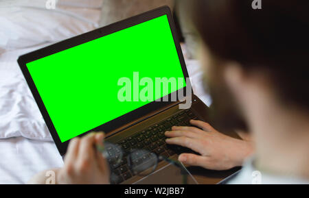 Young man working on his laptop computer connected to wireless internet in his flat. Green screen. Stock Photo