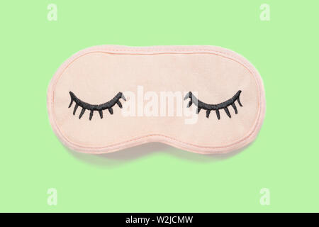 Pastel pink sleep mask with closed eyes embroidered on it with eyelashes on pastel green background. Top view, flat lay. Concept of vivid dreams. Acce Stock Photo