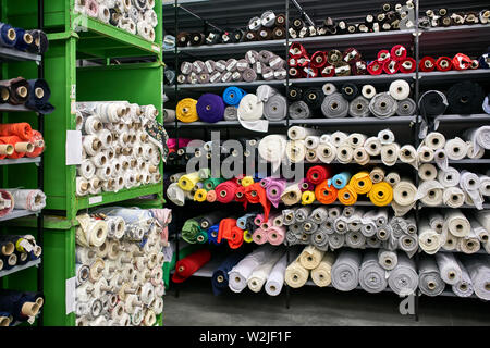 Great warehouse with many shelves with colorful fabric rolls on them. They are white, gray, black, red, pink, orange, blue, cyan, violet, brown, green Stock Photo